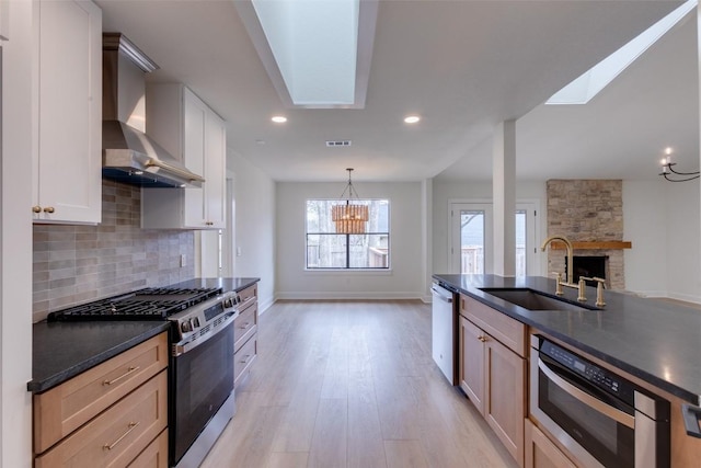 kitchen with wall chimney exhaust hood, a stone fireplace, sink, stainless steel appliances, and backsplash