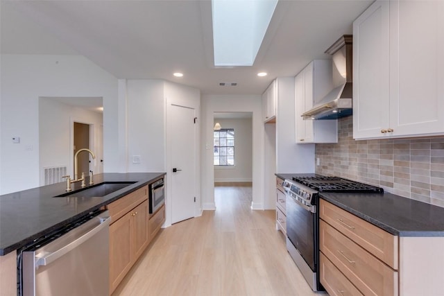 kitchen featuring sink, wall chimney range hood, appliances with stainless steel finishes, white cabinets, and light brown cabinetry