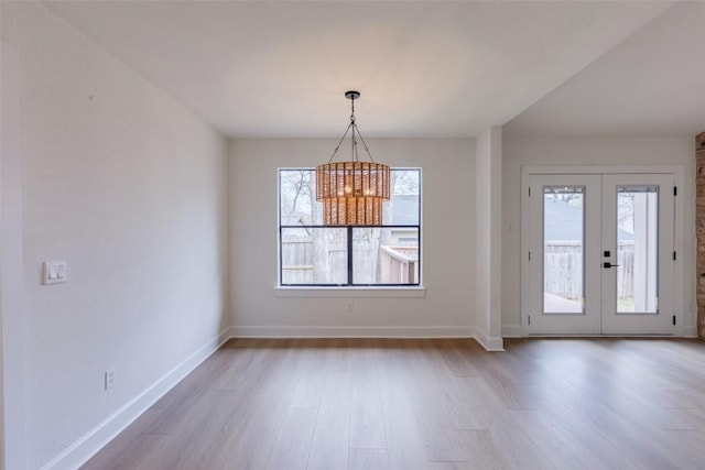 unfurnished dining area with a healthy amount of sunlight, a chandelier, light wood-type flooring, and french doors