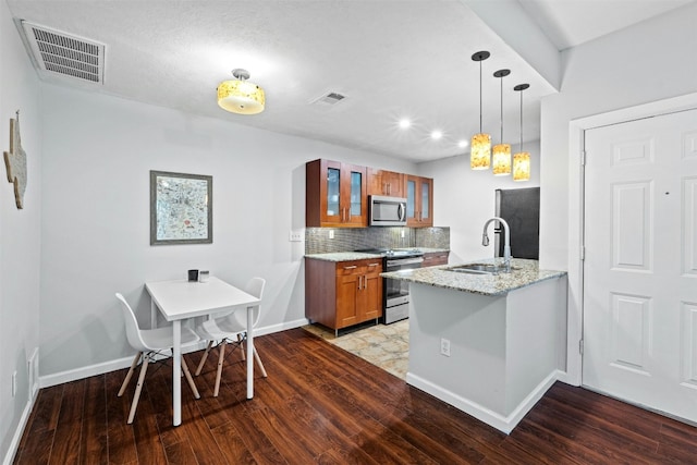 kitchen featuring sink, decorative light fixtures, appliances with stainless steel finishes, kitchen peninsula, and light stone countertops