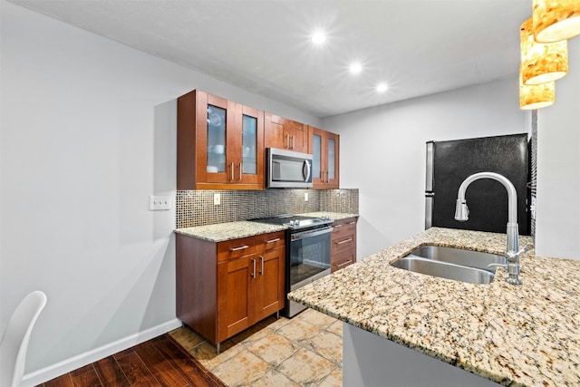 kitchen featuring sink, backsplash, stainless steel appliances, light stone counters, and decorative light fixtures