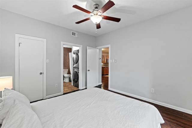 bedroom with ceiling fan, stacked washer and clothes dryer, connected bathroom, and dark hardwood / wood-style flooring