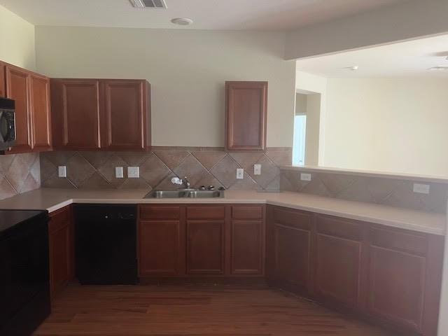 kitchen with tasteful backsplash, dark hardwood / wood-style floors, sink, and black appliances