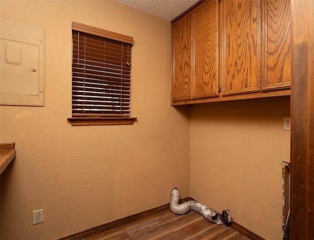 clothes washing area with wood-type flooring, electric panel, cabinets, and a textured ceiling