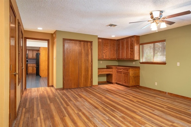 kitchen with built in desk, a textured ceiling, and light wood-type flooring