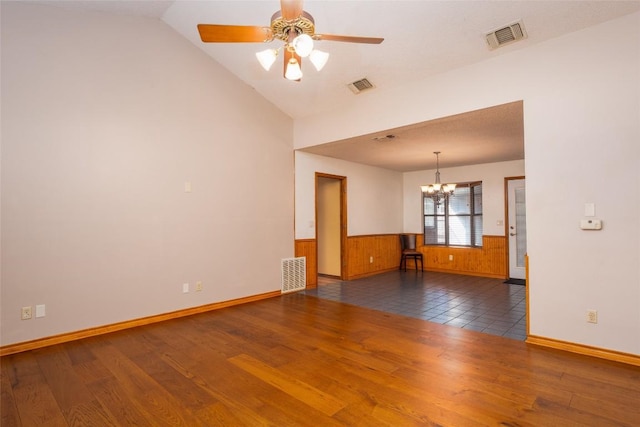 spare room featuring lofted ceiling, ceiling fan with notable chandelier, dark wood-type flooring, and wood walls