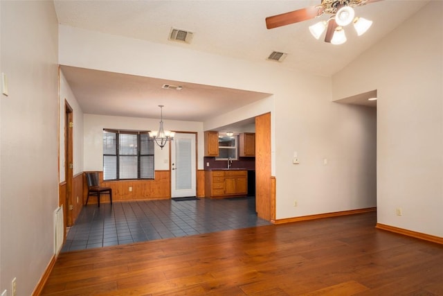 unfurnished living room with sink, dark wood-type flooring, ceiling fan with notable chandelier, and wooden walls