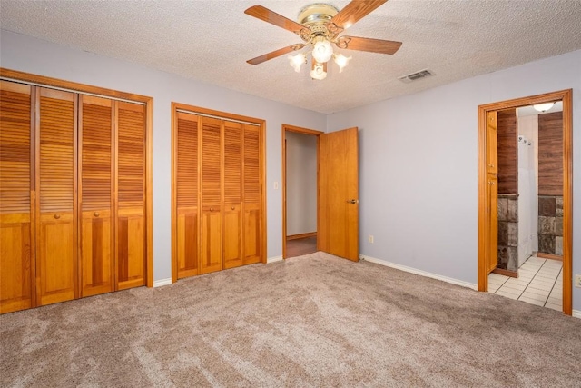 unfurnished bedroom featuring two closets, connected bathroom, light colored carpet, ceiling fan, and a textured ceiling