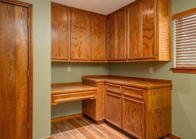 kitchen featuring built in desk, a textured ceiling, and light hardwood / wood-style flooring