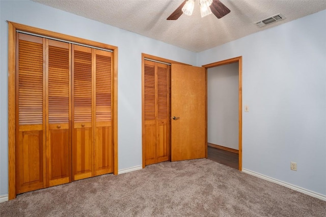 unfurnished bedroom featuring light carpet, ceiling fan, two closets, and a textured ceiling