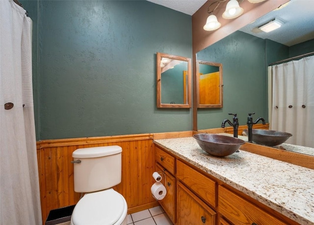 bathroom with tile patterned flooring, vanity, wooden walls, and toilet