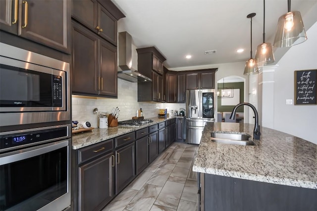 kitchen featuring sink, appliances with stainless steel finishes, pendant lighting, a kitchen island with sink, and wall chimney range hood