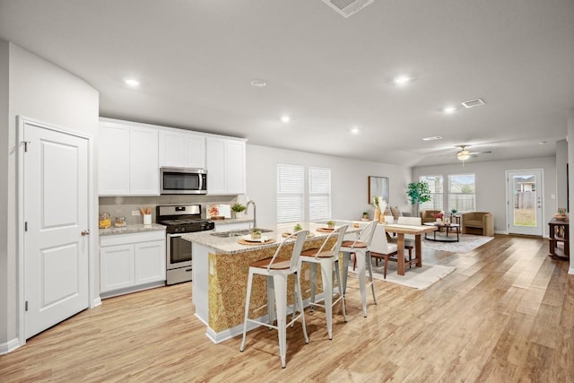 kitchen featuring appliances with stainless steel finishes, a breakfast bar, white cabinetry, a center island with sink, and light wood-type flooring