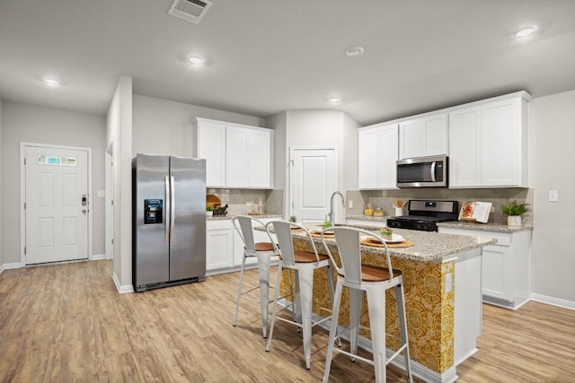 kitchen with stainless steel appliances, a kitchen bar, a center island with sink, and white cabinets