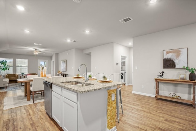 kitchen featuring sink, white cabinetry, light stone counters, dishwasher, and an island with sink