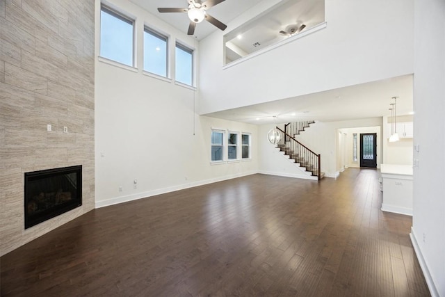 unfurnished living room featuring a tiled fireplace, plenty of natural light, dark hardwood / wood-style floors, and ceiling fan