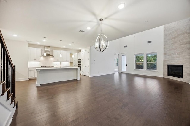 unfurnished living room featuring a tiled fireplace, a notable chandelier, dark wood-type flooring, and a high ceiling