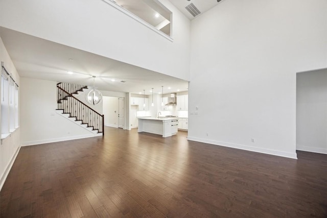 unfurnished living room featuring an inviting chandelier, a towering ceiling, and dark wood-type flooring