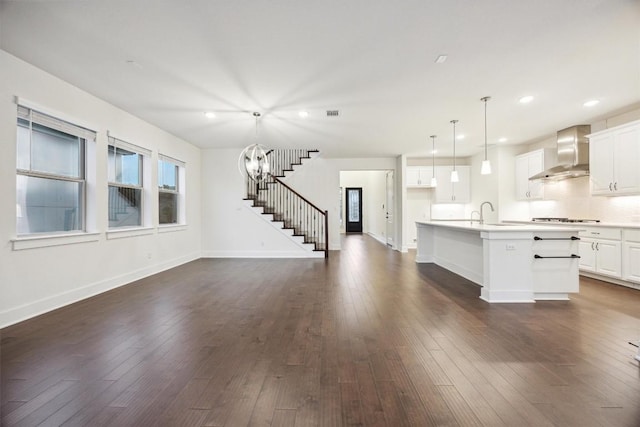 kitchen with gas stovetop, an island with sink, pendant lighting, wall chimney range hood, and white cabinets