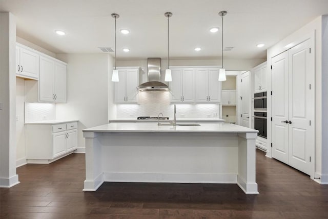 1220 Brassano Pl, Leander, TX 78641 - kitchen with wall chimney range hood, dark wood finished floors, decorative backsplash, white cabinetry, and recessed lighting
