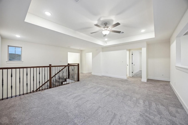 carpeted spare room featuring a raised ceiling and ceiling fan