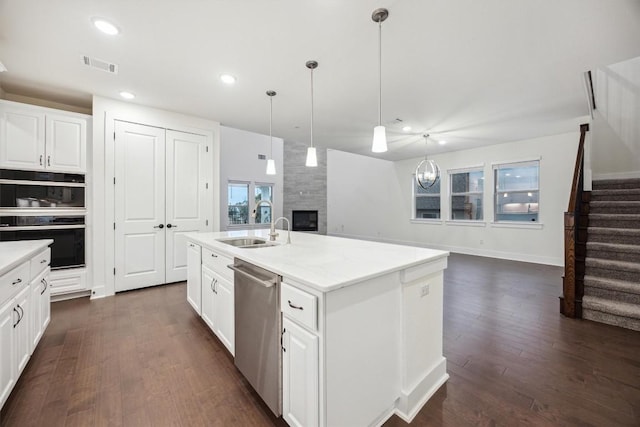 kitchen with decorative light fixtures, dishwasher, a large fireplace, white cabinets, and a center island with sink