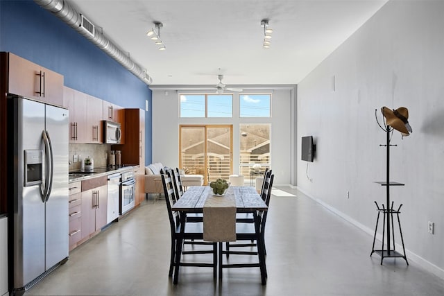 dining space with finished concrete floors, ceiling fan, a towering ceiling, and baseboards