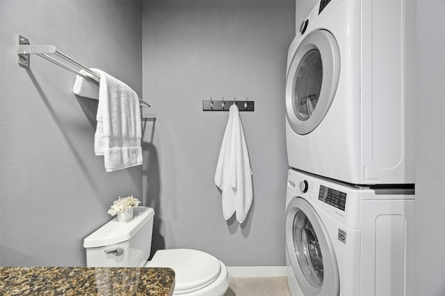 bathroom featuring stacked washer and dryer, toilet, and baseboards