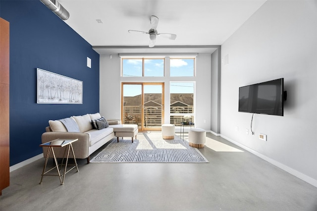 living area featuring finished concrete flooring, a high ceiling, a ceiling fan, and baseboards