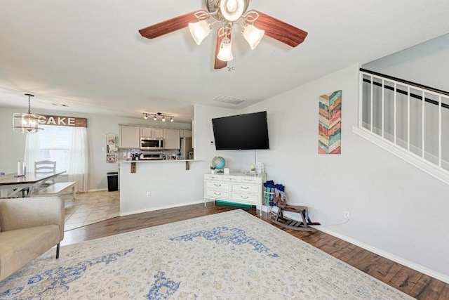 living room with ceiling fan with notable chandelier, rail lighting, and light wood-type flooring