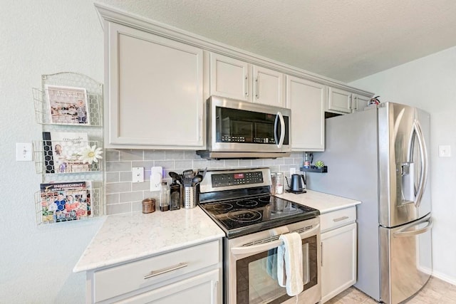 kitchen with light stone counters, backsplash, stainless steel appliances, and a textured ceiling