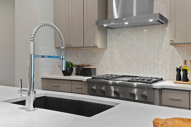 kitchen with sink, wall chimney range hood, gray cabinets, stainless steel gas cooktop, and decorative backsplash