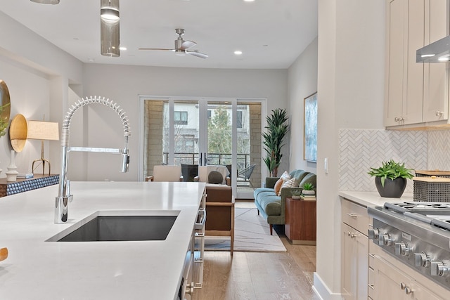 kitchen with sink, wall chimney range hood, tasteful backsplash, light hardwood / wood-style floors, and stainless steel gas stovetop