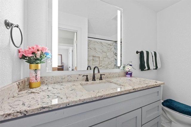 bathroom with vanity, toilet, and tiled shower