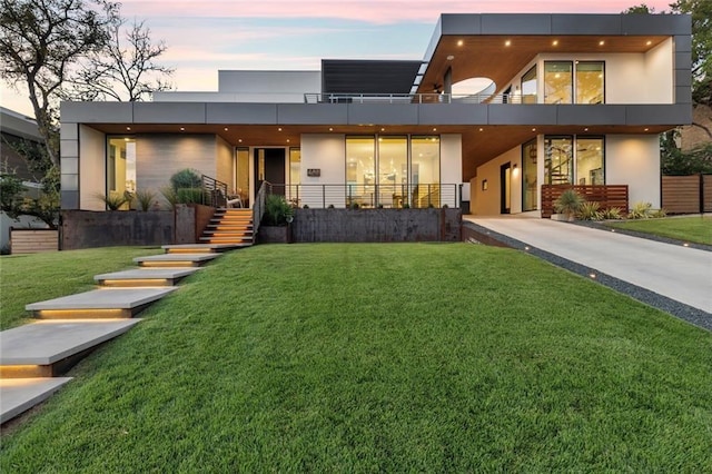 back of house at dusk featuring stairs, a lawn, and stucco siding