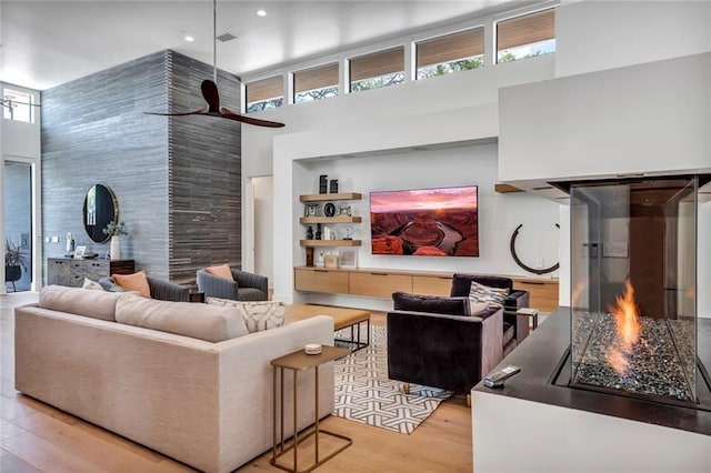 living room featuring light hardwood / wood-style flooring, ceiling fan, and a high ceiling