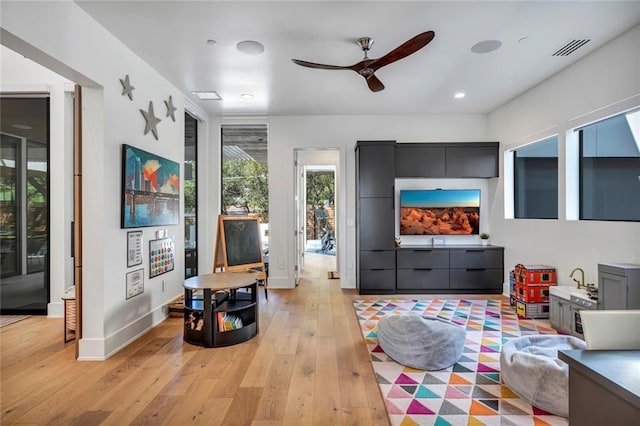 living area featuring baseboards, visible vents, ceiling fan, and light wood finished floors