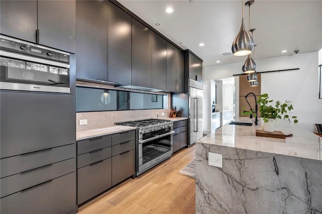 kitchen with pendant lighting, premium appliances, light stone countertops, and sink