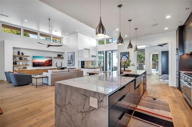 kitchen featuring decorative light fixtures, sink, a large island with sink, ceiling fan, and light stone counters