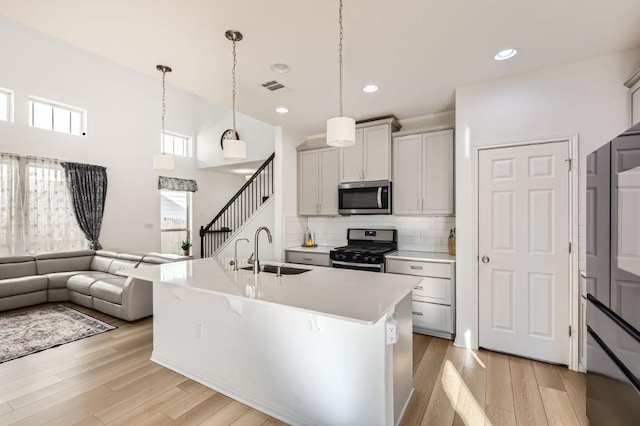 kitchen with sink, gray cabinetry, appliances with stainless steel finishes, pendant lighting, and a kitchen island with sink