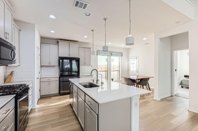 kitchen with sink, gray cabinets, stainless steel appliances, and a center island with sink