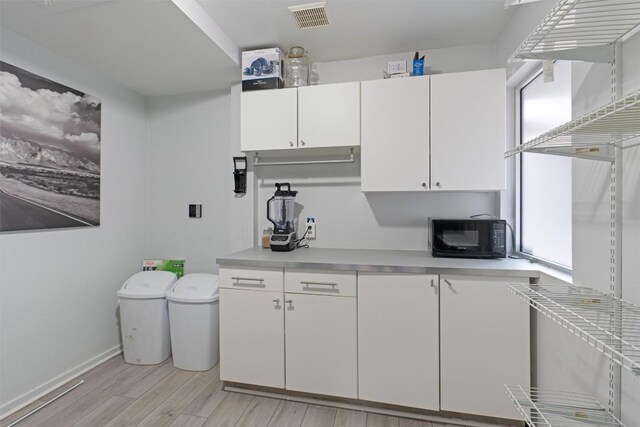 3601 Marcae Ct, Austin, TX 78704 - kitchen featuring black microwave, light countertops, light wood-type flooring, white cabinetry, and baseboards