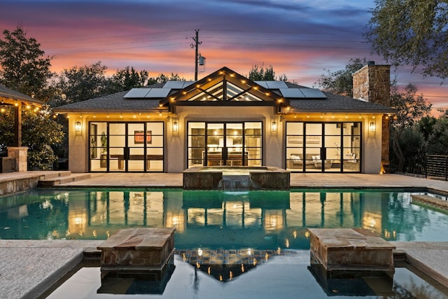 pool at dusk with a patio and an in ground hot tub