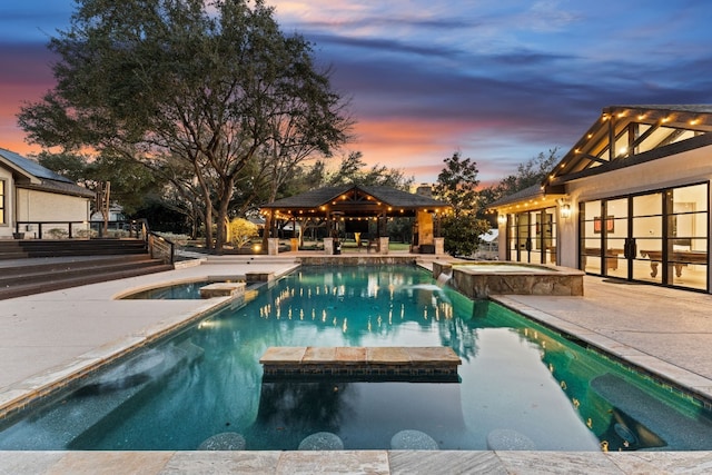 pool at dusk with a gazebo, a patio area, and an in ground hot tub