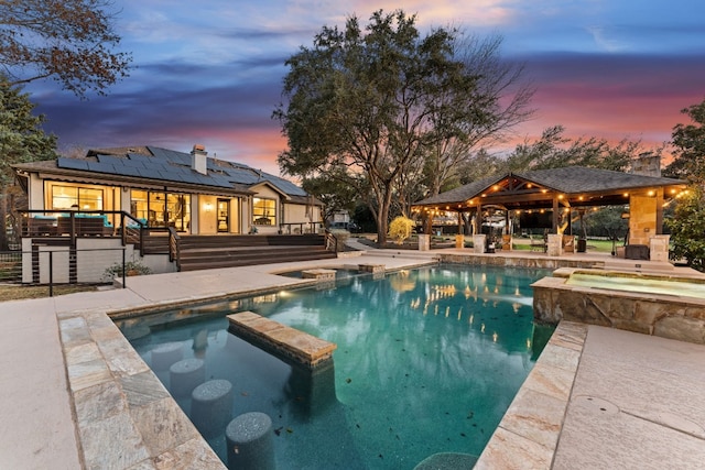 pool at dusk featuring a gazebo, a patio area, and an in ground hot tub