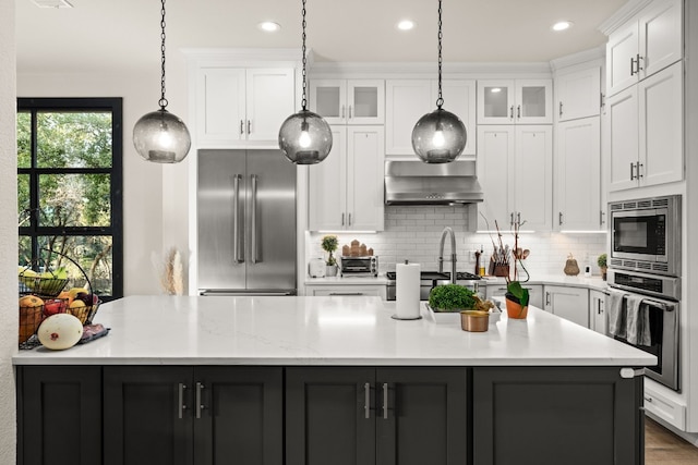 kitchen featuring built in appliances, exhaust hood, white cabinets, and a center island with sink