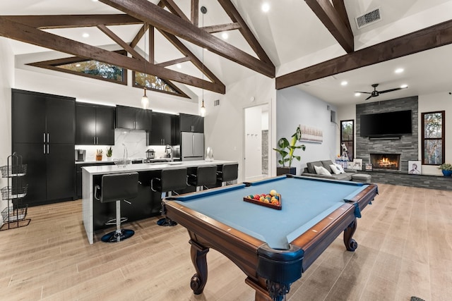 rec room featuring a stone fireplace, high vaulted ceiling, beam ceiling, and light hardwood / wood-style flooring