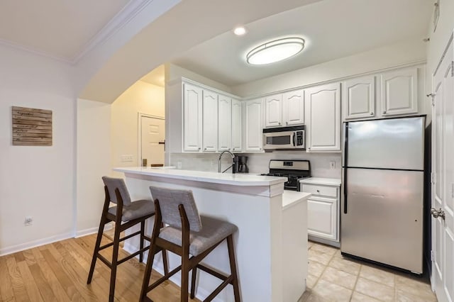 kitchen featuring a breakfast bar, white cabinetry, kitchen peninsula, stainless steel appliances, and crown molding