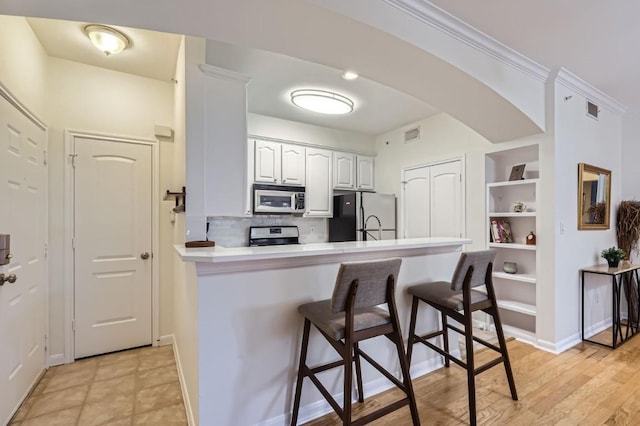 kitchen with a breakfast bar, appliances with stainless steel finishes, white cabinets, decorative backsplash, and kitchen peninsula