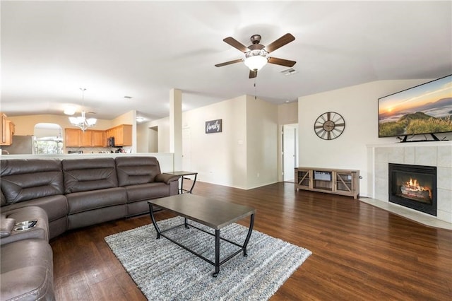 living room with lofted ceiling, ceiling fan with notable chandelier, a tile fireplace, and dark hardwood / wood-style floors